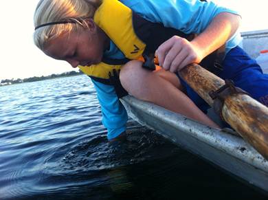 Closeup photo of a volunteer leaning over the side of a boat to collect a sample of water